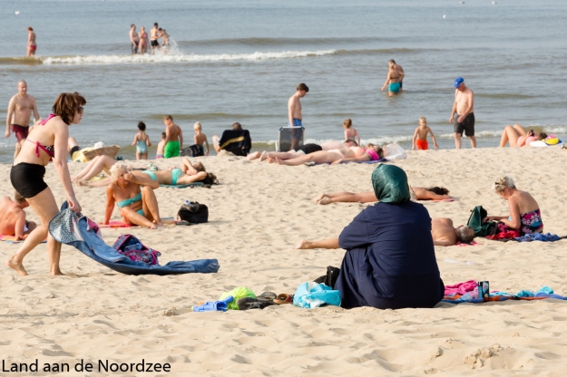 Nederland, The Netherlands, Kijkduin 15-09-2016 Drukte op het strand tijdens de ongewoon hete septemberdagen. Veel mensen zoeken verkoeling aan de kust. Een moslimvrouw zit gekleed in een bedekkend gewaad en met hoofddoek op het strand. Foto: Bert Spiertz
